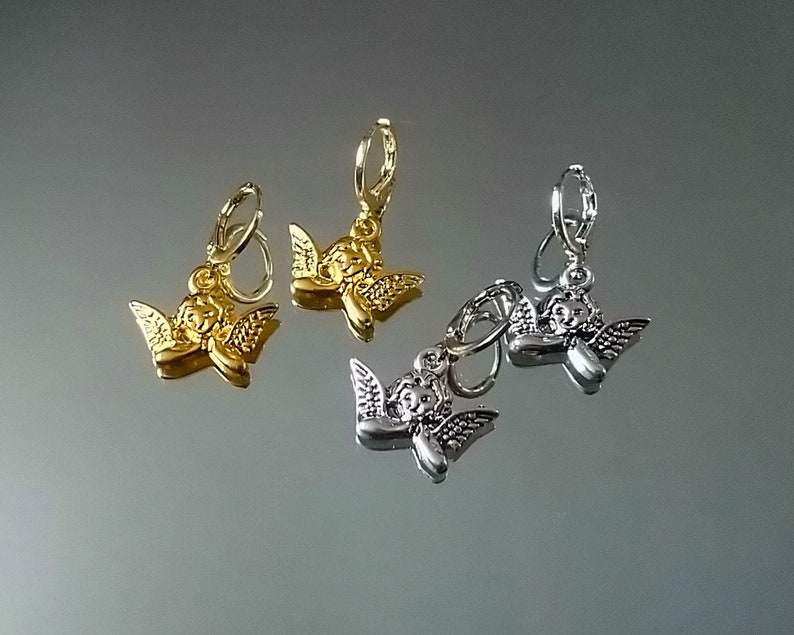 May include: Three pairs of angel charm earrings. Two pairs are silver and one pair is gold.