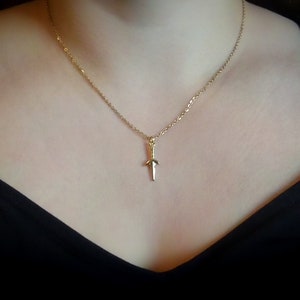 May include: A gold chain necklace with a small gold dagger pendant.