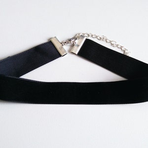 Könnte beinhalten: Eine schwarze Samt-Choker-Kette mit einer silbernen Kette und einem Verschluss.