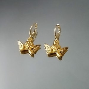 May include: A pair of gold angel charm earrings with a hoop design. The charms are detailed with a cherub face and wings.