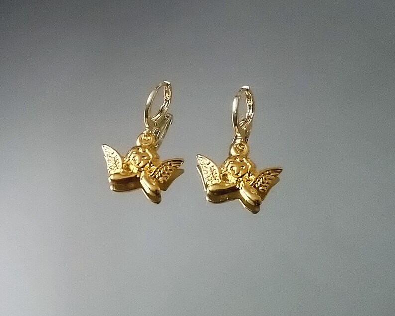 May include: A pair of gold angel charm earrings with a hoop design. The charms are detailed with a cherub face and wings.