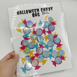 May include: A white sheet of paper with the text "Halloween Candy Bag" and the words "Total $2.50 HOLDMYMONEY" printed on it. The paper is decorated with 20 holographic candy stickers in various colors.