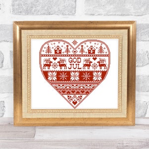 May include: A framed cross-stitch design of a red heart with Scandinavian Christmas motifs, including snowflakes, reindeer, and houses. The text "GOD JUL" is embroidered in the centre of the heart.