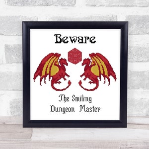 Könnte beinhalten: Ein gerahmter Druck mit weißem Hintergrund und schwarzem Rahmen. Der Druck zeigt einen roten und gelben Drachen mit einem roten 20-seitigen Würfel in der Mitte. Der Text "Beware The Smiling Dungeon Master" ist unter dem Drachen gedruckt.