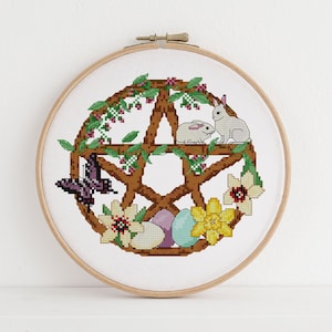 May include: A cross-stitch embroidery hoop with a brown pentagram surrounded by green vines, white bunnies, purple butterfly, yellow flowers, and pastel colored eggs.