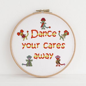 May include: Embroidered hoop art with a white background and colorful pixelated characters. The text reads "Dance your cares away".