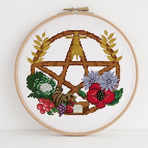 Puede incluir: Un diseño de bordado de punto de cruz que presenta un pentáculo con una figura humana estilizada en su interior, rodeado de espigas de trigo, una amapola, una col, uvas y una hogaza de pan.