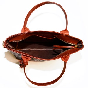 Op de afbeelding: Een bruine leren tote bag met een ritssluiting en een bovenste handvat. De tas is open en de binnenkant is gevoerd met een bruine stof.