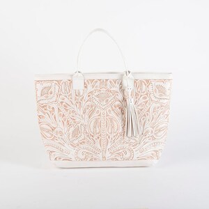 May include: White leather tote bag with a floral embossed design. The bag has a top handle and a tassel.