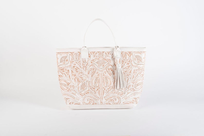 May include: White leather tote bag with a floral embossed design. The bag has a top handle and a tassel.