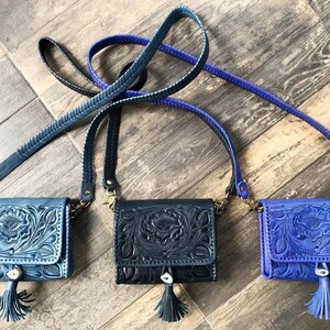 May include: Three small leather purses with intricate floral designs. The purses are blue, black, and purple and have a tassel on the bottom.