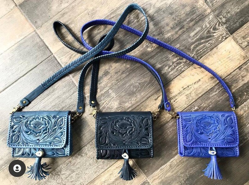 May include: Three small leather purses with intricate floral designs. The purses are blue, black, and purple and have a tassel on the bottom.
