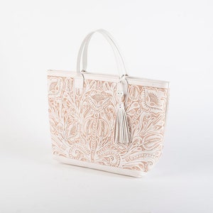 May include: A white leather tote bag with a floral design. The bag has a top handle and a tassel.