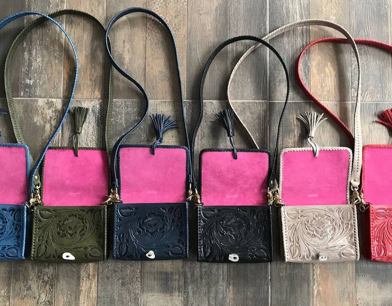 May include: Five small leather purses with floral embossed designs. Each purse has a pink lining and a long strap with a tassel. The purses are in different colors: green, navy blue, black, beige, and red.