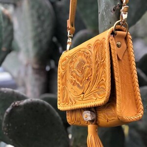 May include: A small, mustard yellow leather purse with intricate floral tooling. The purse has a long strap and a tassel.