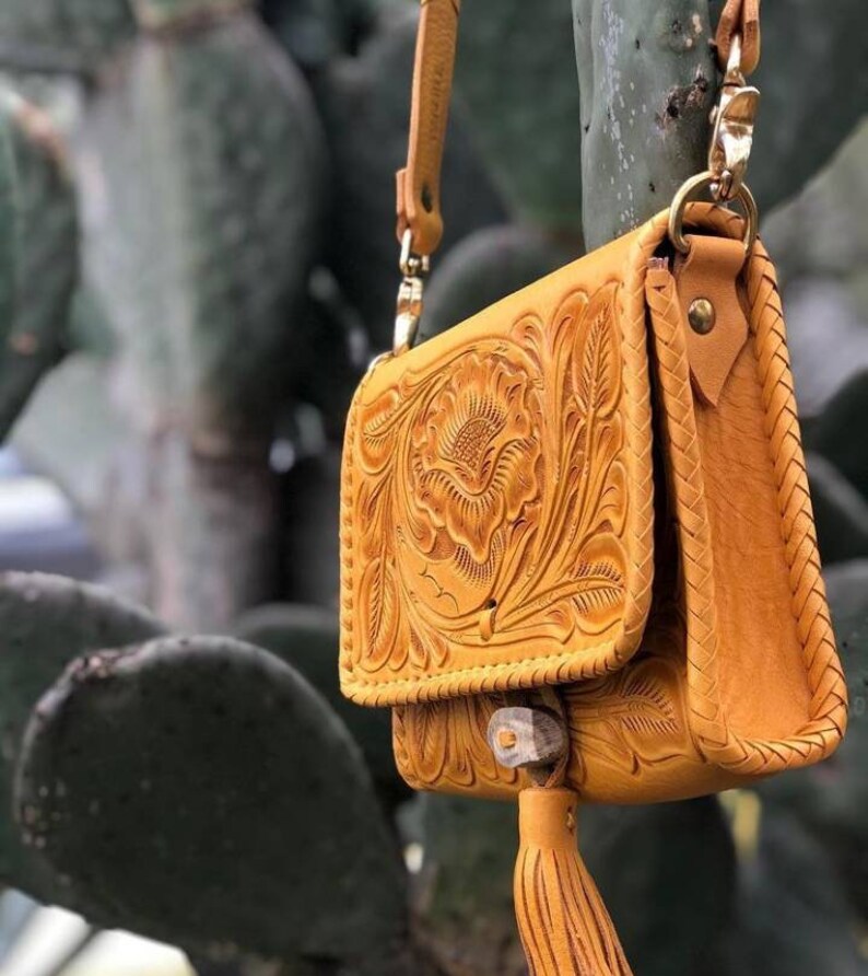 May include: A small, mustard yellow leather purse with intricate floral tooling. The purse has a long strap and a tassel.