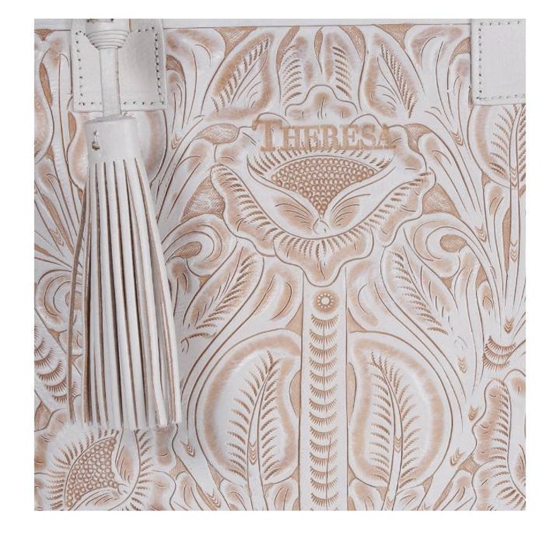 May include: White leather tote bag with an embossed floral design and the word "THERESA" in the center. The bag has a white tassel.