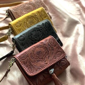 May include: Four leather purses with floral embossed designs. The purses are in brown, black, yellow, and a lighter brown. Each purse has a strap and a tassel.