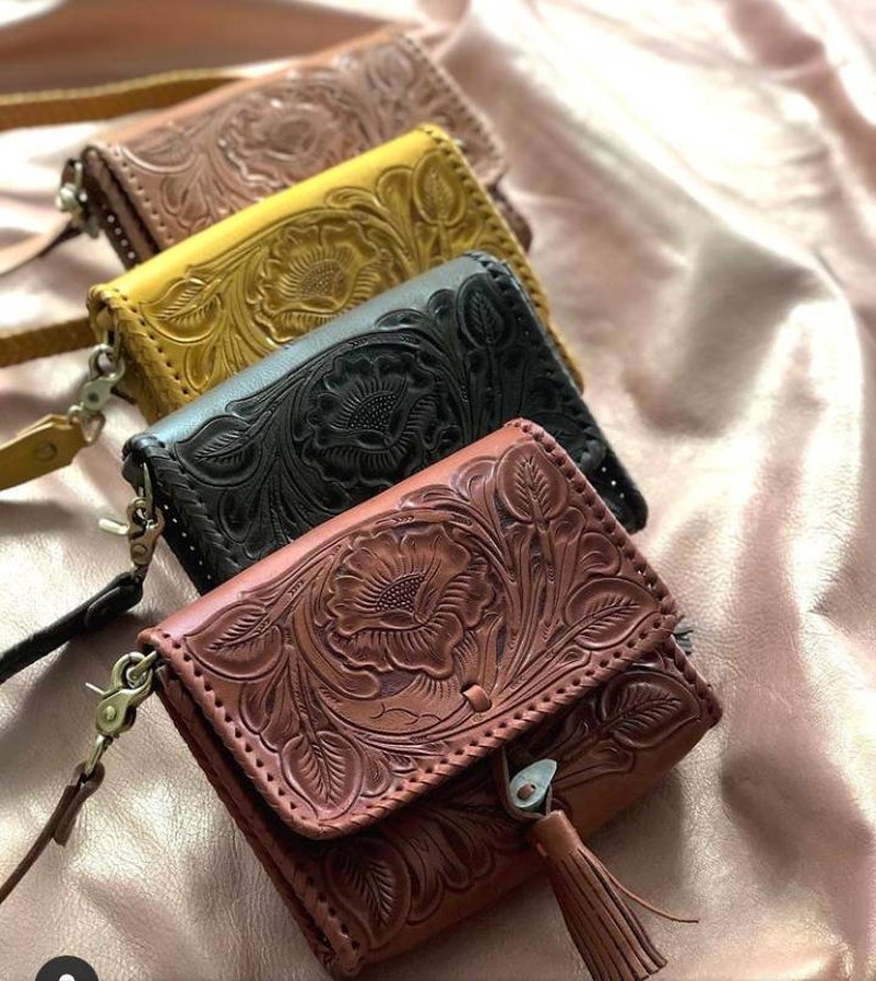 May include: Four leather purses with floral embossed designs. The purses are in brown, black, yellow, and a lighter brown. Each purse has a strap and a tassel.