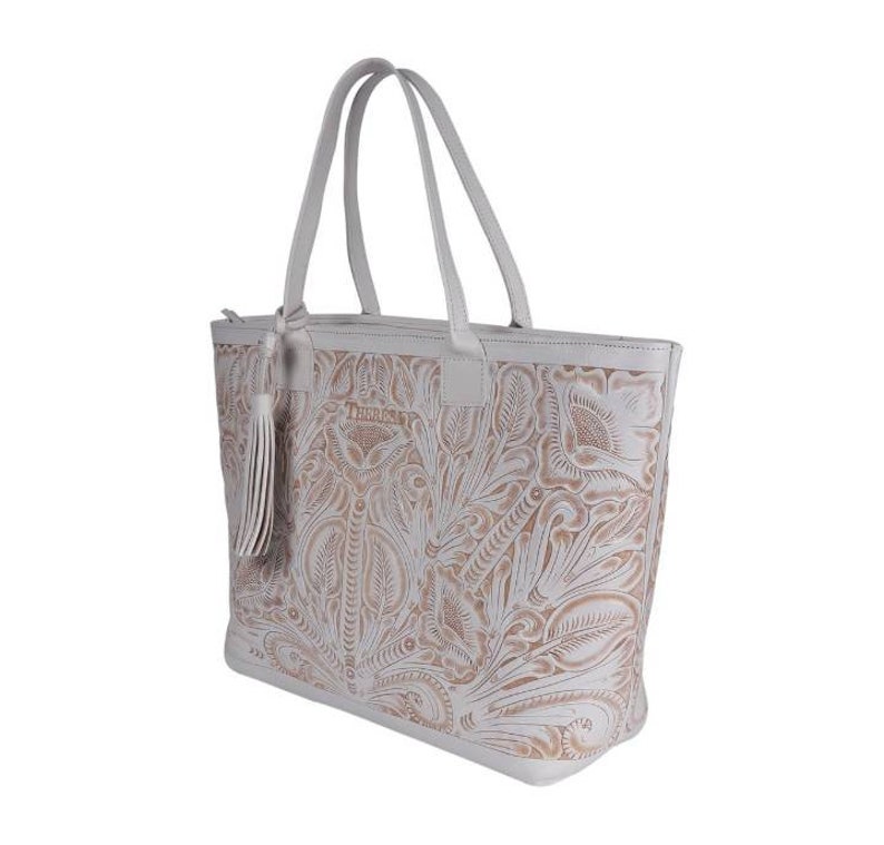May include: White leather tote bag with a floral embossed design. The bag has a zipper closure and a tassel on the front. The brand name "The Sak" is embossed on the front of the bag.