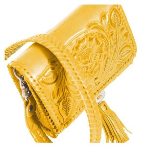 May include: A yellow leather handbag with a floral embossed design and a tassel. The bag has a braided strap and a zipper closure.