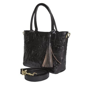 May include: Black leather tote bag with an intricate floral design and a tassel. The bag has a top handle and a detachable shoulder strap.