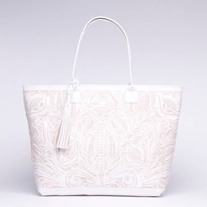 May include: White leather tote bag with an embossed floral design. The bag has a top zipper closure and a tassel.