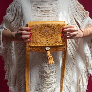 May include: A yellow leather crossbody bag with a floral design and a tassel. The bag has a long strap and a flap closure.