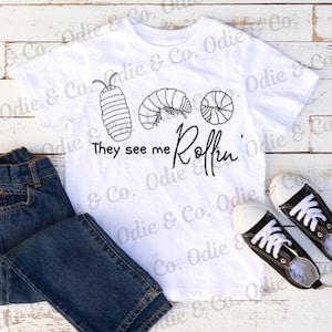 Puede incluir: Camiseta blanca con un gráfico negro de tres cochinillas y el texto "They see me Rollin'"