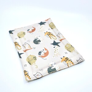 May include: A beige cat bed with a white background and a pattern of colourful cats and stars. The cats are in various poses, including sleeping, sitting, and standing. The stars are in a variety of sizes and colours.