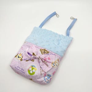 May include: A pink and blue fabric hanging pouch with a blue plush lining. The pouch features a bow and a repeating pattern of cartoon characters with the text "Love You Friend of Duffy" and "Friend of Duffy".
