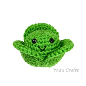 May include: A green crocheted plush toy shaped like a head of cabbage with a smiling face and black eyes.