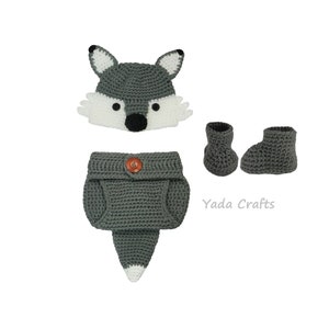 May include: Gray crocheted baby outfit with a wolf hat, diaper cover, and booties. The hat has white accents and a black nose. The diaper cover has a brown button. The booties are gray.