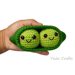 May include: Two green crocheted peas with smiling faces inside a green crocheted pea pod.