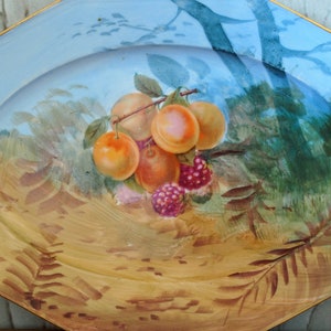 May include: A blue and gold oval serving platter with a painted design of fruit and leaves. The fruit includes peaches and raspberries.