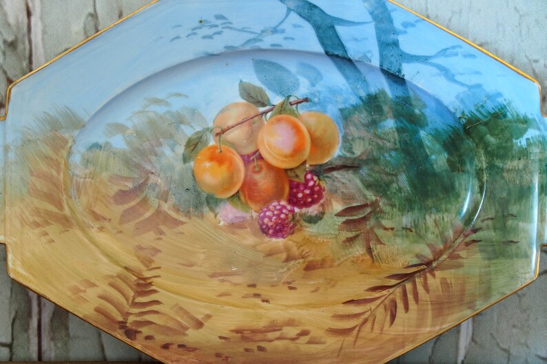May include: A blue and gold oval serving platter with a painted design of fruit and leaves. The fruit includes peaches and raspberries.