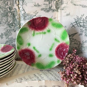 Puede incluir: Un juego de platos de porcelana blanca vintage con un diseño en relieve de rosas rojas y hojas verdes. Los platos están apilados uno encima del otro y están sobre una hoja de música.
