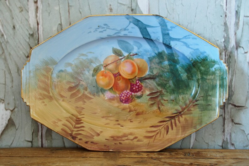 May include: A vintage octagonal ceramic serving platter with a blue and yellow glaze. The platter features a hand-painted design of a branch of fruit with peaches and raspberries.