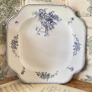 Könnte beinhalten: Eine weiße quadratische Servierplatte mit einem blauen Blumendesign. Die Platte hat einen gewellten Rand und einen erhöhten Rand.