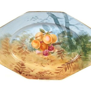 May include: Octagonal porcelain serving platter with a blue and gold rim. The platter features a hand-painted scene of a tree branch with fruit and berries.