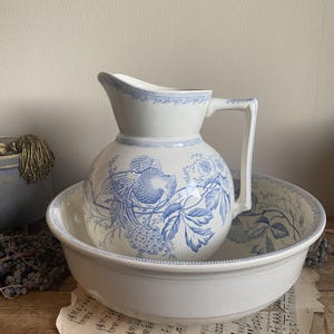 Może przedstawiać: Zestaw ceramiczny dzbanek i miska z niebieskim wzorem kwiatowym. Dzbanek ma okrągłe ciało i zakrzywiony dzióbek. Miska jest okrągła i ma szeroki rant.