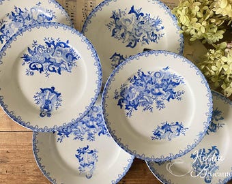 Op de afbeelding: Set van zes blauwe en witte porseleinen borden met een delicaat bloemenpatroon en cherubijnenfiguren. De borden hebben een gegolfde rand en een witte achtergrond.