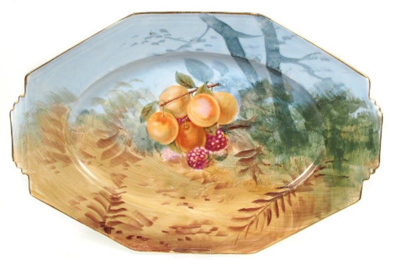May include: A blue and white oval serving platter with a gold rim. The platter features a painted scene of a branch of fruit with peaches and raspberries, set against a background of trees and foliage.