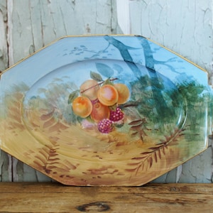 May include: A vintage octagonal porcelain serving platter with a hand-painted design of fruit and foliage. The platter features a blue background with a yellow rim and a central image of peaches, berries, and leaves.
