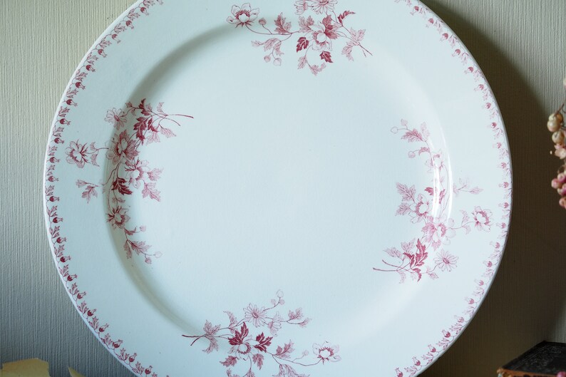 May include: A large white ceramic plate with a pink floral design around the rim. The plate has a scalloped edge and a raised centre.