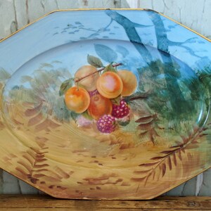 May include: Octagonal ceramic serving platter with a blue and gold rim. The platter features a hand-painted design of peaches and raspberries on a branch with green leaves.