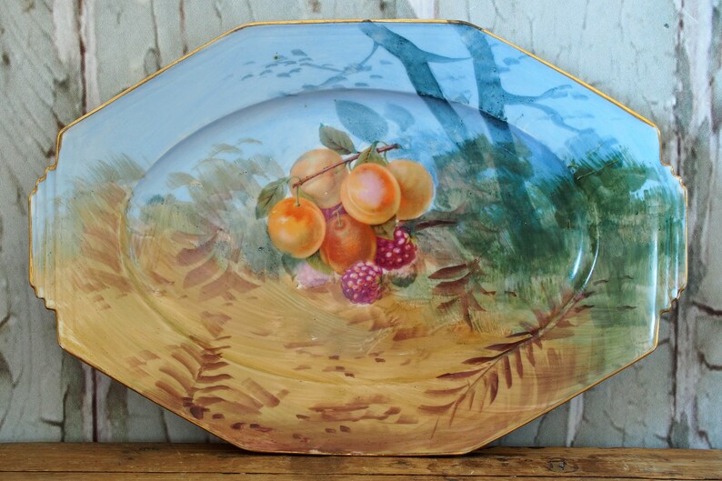 May include: Octagonal ceramic serving platter with a blue and gold rim. The platter features a hand-painted design of peaches and raspberries on a branch with green leaves.