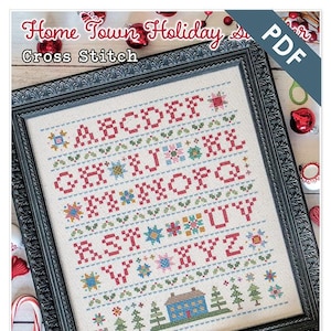Könnte beinhalten: Ein Kreuzstichmuster mit einem bunten Alphabet, einem kleinen Haus und Bäumen. Das Muster trägt den Titel "Home Town Holiday" und wurde von Lori Holt für Bee in my Bonnet Co. entworfen.