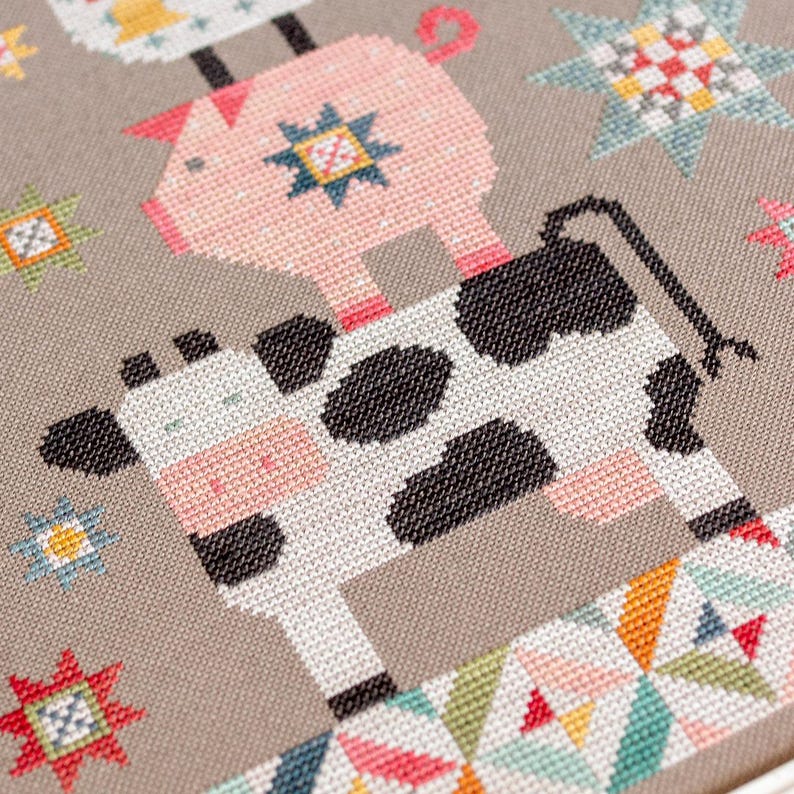 May include: A cross-stitch design depicting a cow, pig, and chicken in a stack. The cow is white with black patches, the pig is pink, and the chicken is yellow. The background is grey, with colourful star and geometric patterns.