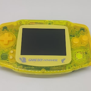 Könnte beinhalten: Eine gelbe, transparente Game Boy Advance Handheld-Videospielkonsole mit einem schwarzen Bildschirm. Die Konsole hat ein gelbes Tastenfeld und der Text "GAME BOY ADVANCE" ist auf der Vorderseite aufgedruckt.